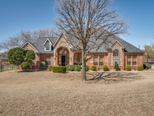 view of front of house featuring brick siding, fence, and roof with shingles