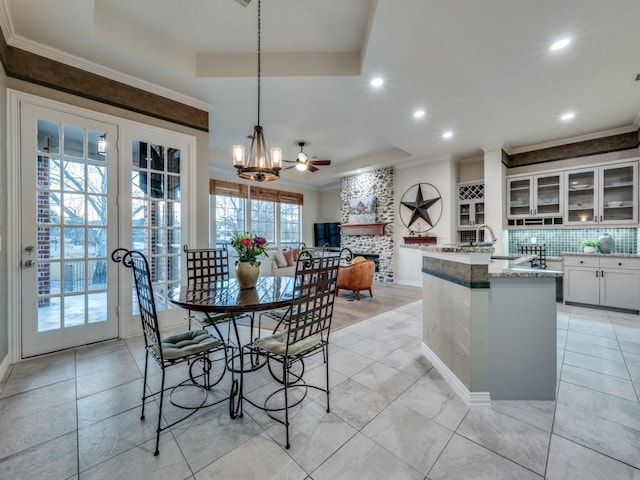 dining space featuring a large fireplace, french doors, a tray ceiling, and ornamental molding