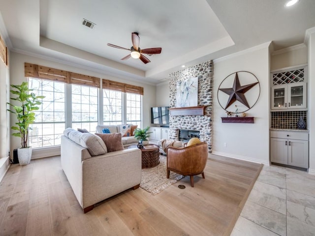 living room featuring a large fireplace, visible vents, baseboards, a tray ceiling, and crown molding