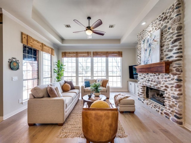 living area featuring a stone fireplace, wood finished floors, visible vents, baseboards, and a tray ceiling