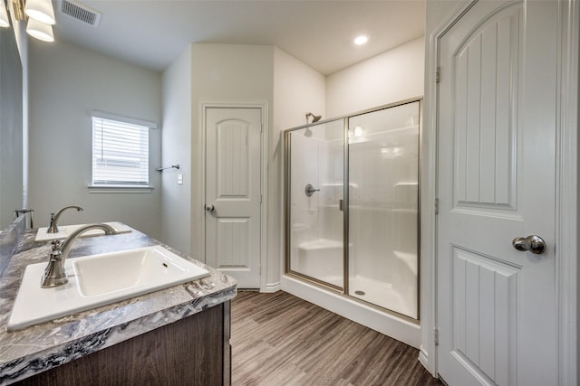 bathroom with visible vents, a sink, a shower stall, and wood finished floors