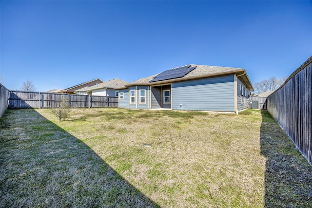 rear view of house with a fenced backyard, a lawn, and solar panels