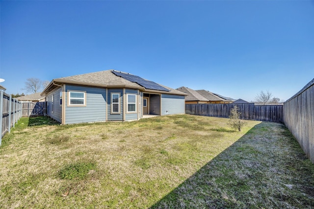 back of house with a lawn, a fenced backyard, and roof mounted solar panels