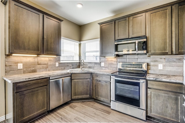 kitchen with light wood-style flooring, a sink, light stone countertops, stainless steel appliances, and backsplash