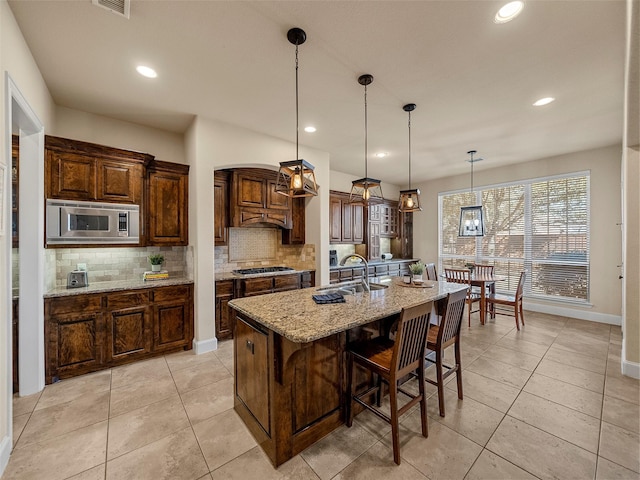 kitchen featuring an island with sink, a sink, light stone countertops, stainless steel appliances, and backsplash