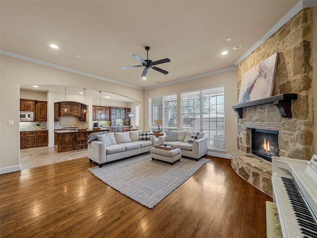 living room featuring light wood finished floors, ceiling fan, a fireplace, and crown molding