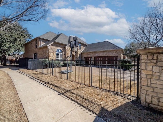 view of front of property with concrete driveway, brick siding, a fenced front yard, and a shingled roof