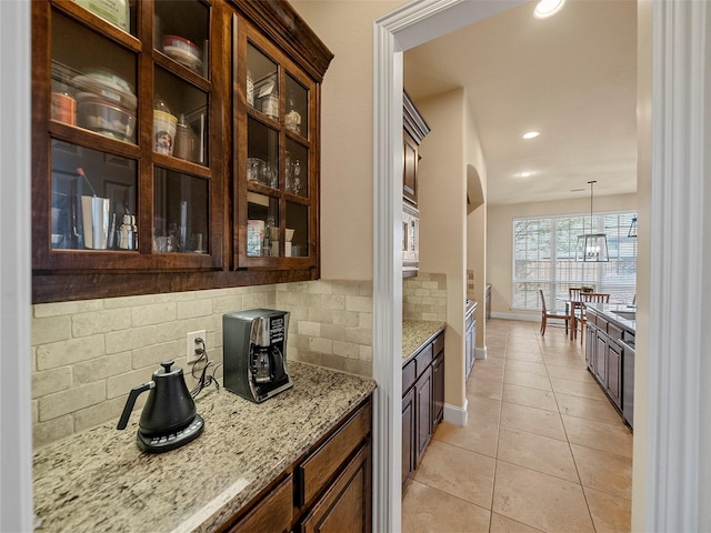 kitchen with light tile patterned floors, tasteful backsplash, glass insert cabinets, light stone countertops, and baseboards