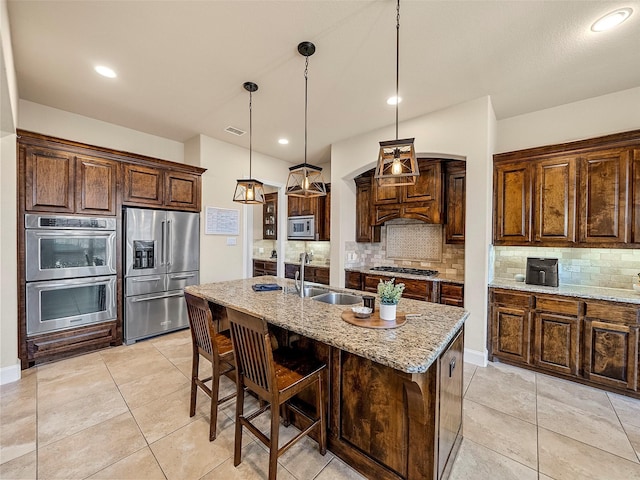 kitchen featuring tasteful backsplash, an island with sink, appliances with stainless steel finishes, light stone countertops, and a sink