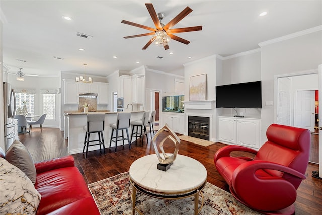living room featuring visible vents, ornamental molding, ceiling fan with notable chandelier, dark wood finished floors, and recessed lighting