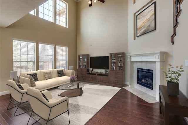 living area with a tile fireplace, a high ceiling, wood finished floors, a ceiling fan, and baseboards