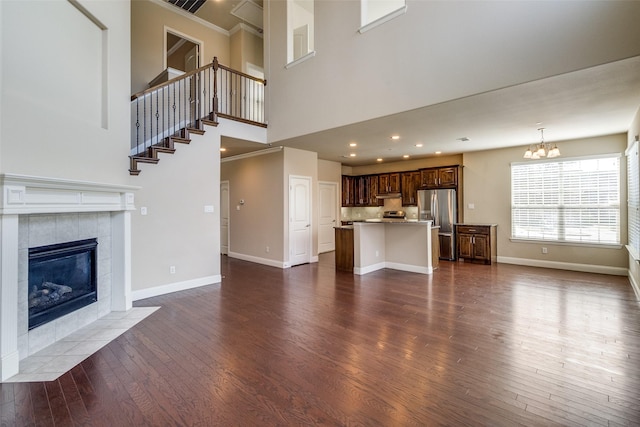 unfurnished living room with a tile fireplace, a high ceiling, baseboards, and dark wood-style flooring