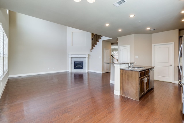 kitchen with light stone counters, a sink, a kitchen island with sink, dishwasher, and visible vents