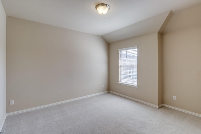 empty room featuring baseboards, lofted ceiling, and light colored carpet