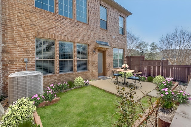 rear view of house featuring fence, a yard, central air condition unit, a patio area, and brick siding