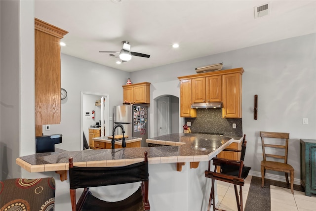 kitchen featuring arched walkways, decorative backsplash, freestanding refrigerator, a peninsula, and a kitchen bar