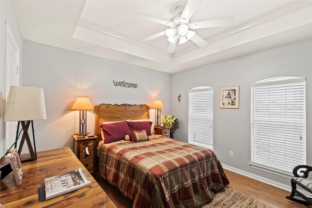 bedroom with a ceiling fan, baseboards, a raised ceiling, and wood finished floors