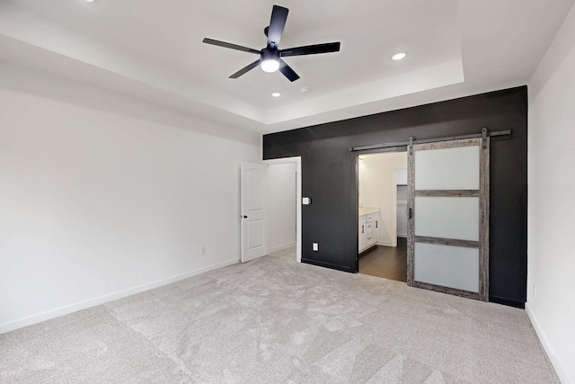 unfurnished bedroom with carpet floors, recessed lighting, a raised ceiling, a barn door, and baseboards