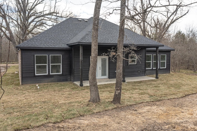 view of front facade with a shingled roof, a front lawn, and a patio