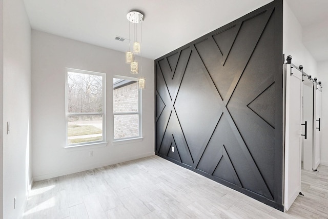 unfurnished room featuring light wood finished floors, a barn door, and visible vents