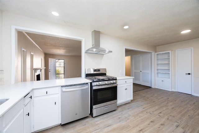 kitchen featuring a textured ceiling, white cabinetry, light wood-style floors, appliances with stainless steel finishes, and wall chimney range hood