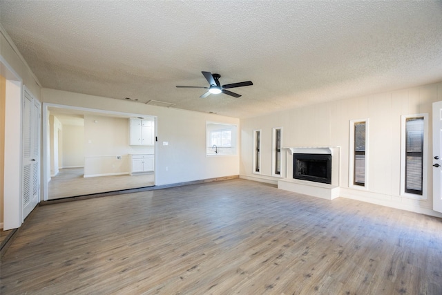 unfurnished living room with a ceiling fan, wood finished floors, a fireplace with raised hearth, and a textured ceiling