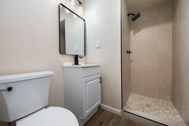 bathroom featuring tiled shower, toilet, wood finished floors, and vanity