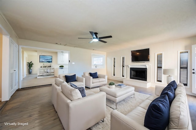 living area featuring ceiling fan, visible vents, a fireplace with raised hearth, and wood finished floors
