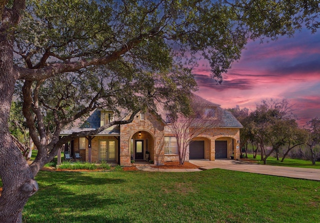 view of front of home featuring an attached garage, a yard, french doors, concrete driveway, and stone siding