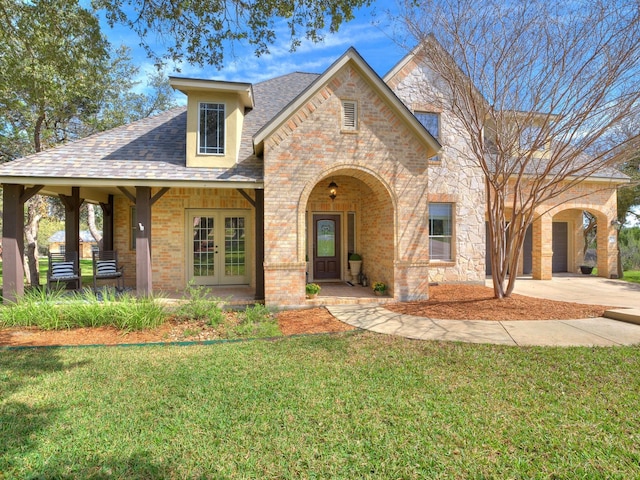 view of front of home with brick siding, a shingled roof, concrete driveway, french doors, and a front yard