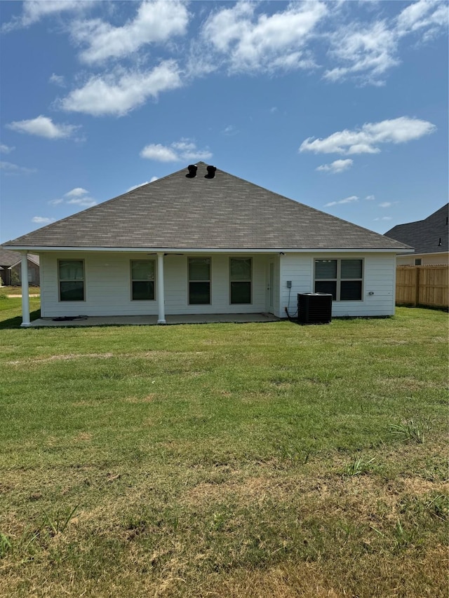 rear view of property featuring a shingled roof, cooling unit, and a lawn