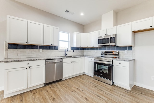 kitchen with a sink, white cabinetry, visible vents, appliances with stainless steel finishes, and light stone countertops