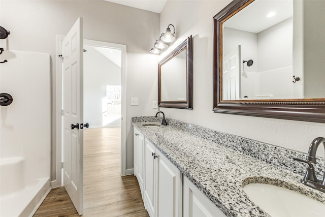 full bathroom with double vanity, walk in shower, a sink, and wood finished floors