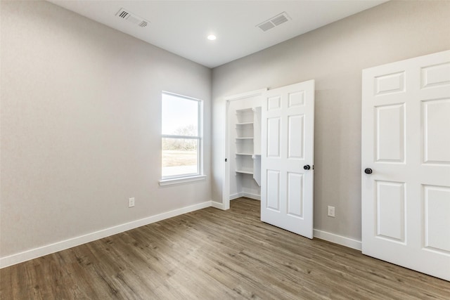 unfurnished bedroom with a walk in closet, wood finished floors, visible vents, and baseboards