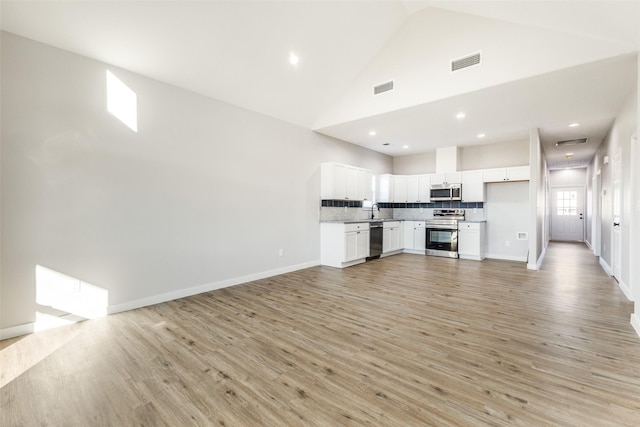 unfurnished living room with a sink, light wood-style floors, visible vents, and high vaulted ceiling