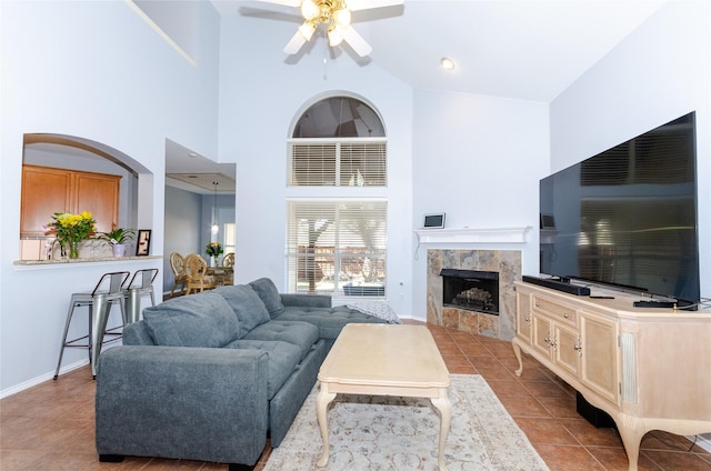 tiled living room with a towering ceiling, baseboards, a ceiling fan, and a tile fireplace