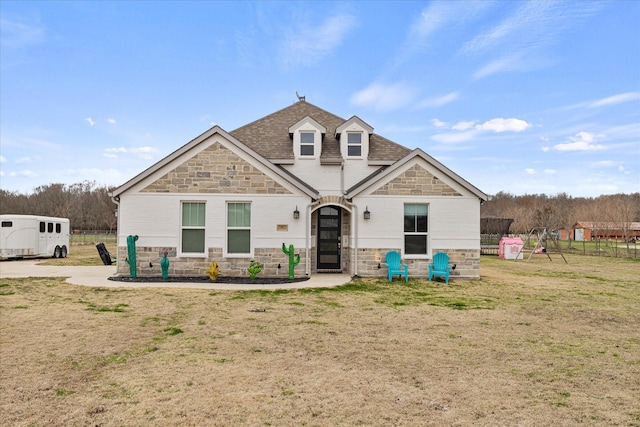 view of front of home featuring stone siding, roof with shingles, a front yard, and fence