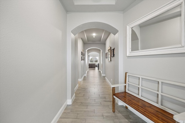 corridor featuring light wood finished floors, baseboards, arched walkways, and a tray ceiling