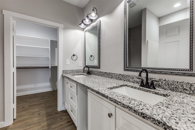 full bathroom with double vanity, a sink, baseboards, and wood finished floors