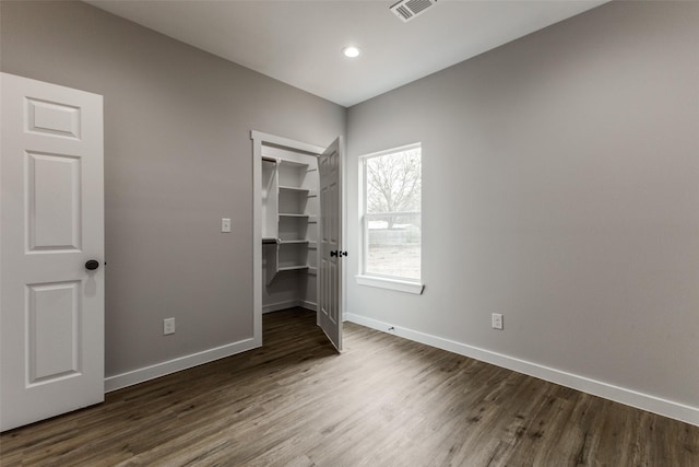 unfurnished bedroom featuring baseboards, visible vents, wood finished floors, a walk in closet, and a closet