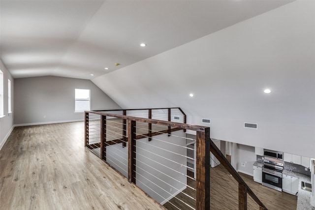 additional living space featuring light wood-type flooring, visible vents, vaulted ceiling, and baseboards