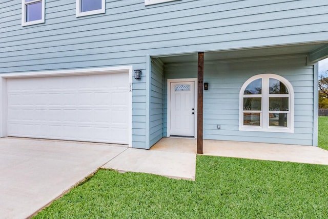 entrance to property featuring an attached garage and a lawn