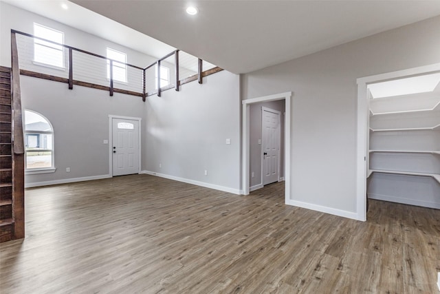 unfurnished living room featuring a wealth of natural light, a towering ceiling, baseboards, and wood finished floors