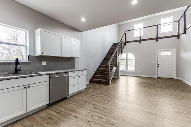 kitchen featuring tasteful backsplash, stainless steel dishwasher, a sink, light wood-type flooring, and plenty of natural light