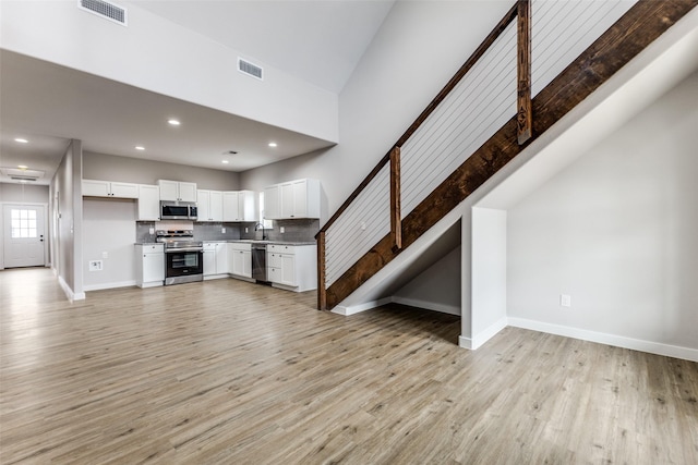 unfurnished living room with baseboards, visible vents, light wood finished floors, and stairs