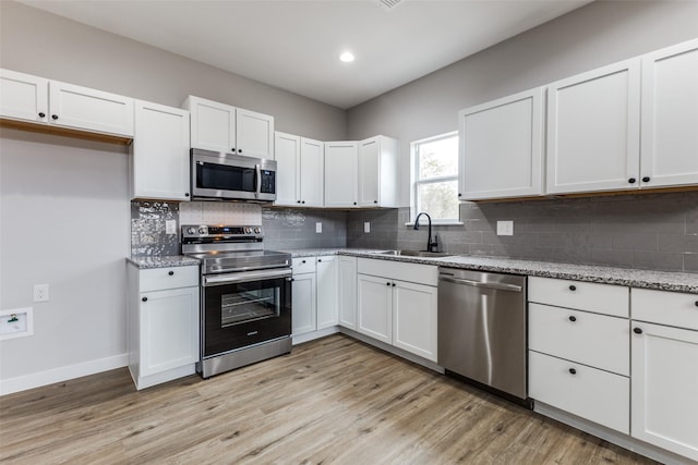 kitchen featuring stainless steel appliances, a sink, white cabinetry, light wood-style floors, and tasteful backsplash