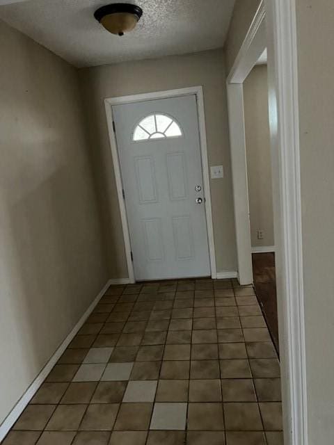 doorway featuring light tile patterned flooring, a textured ceiling, and baseboards