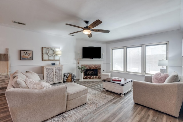 living room featuring visible vents, a ceiling fan, wood finished floors, crown molding, and a fireplace