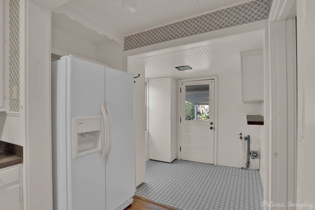 interior space featuring dark countertops, white fridge with ice dispenser, and white cabinets