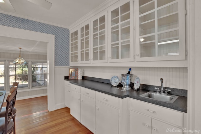 kitchen with crown molding, dark countertops, white cabinets, a sink, and wallpapered walls